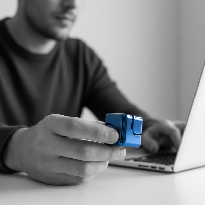 Person at a desk quietly fidgeting with the blue metal fidget cube, cube in colour against a black-and-white scene