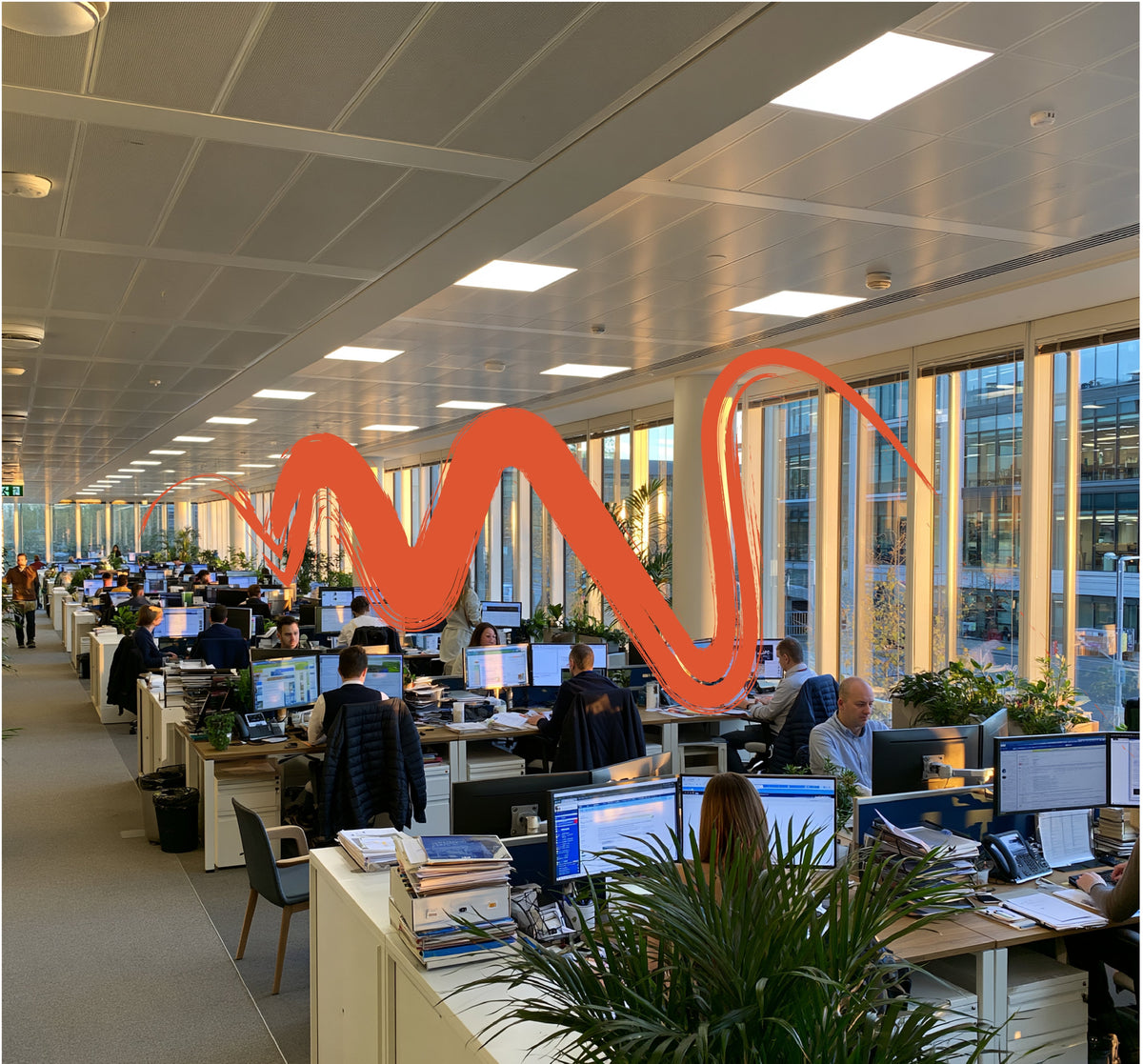 Open-plan office with people working at rows of desks beneath a large orange wave scribble