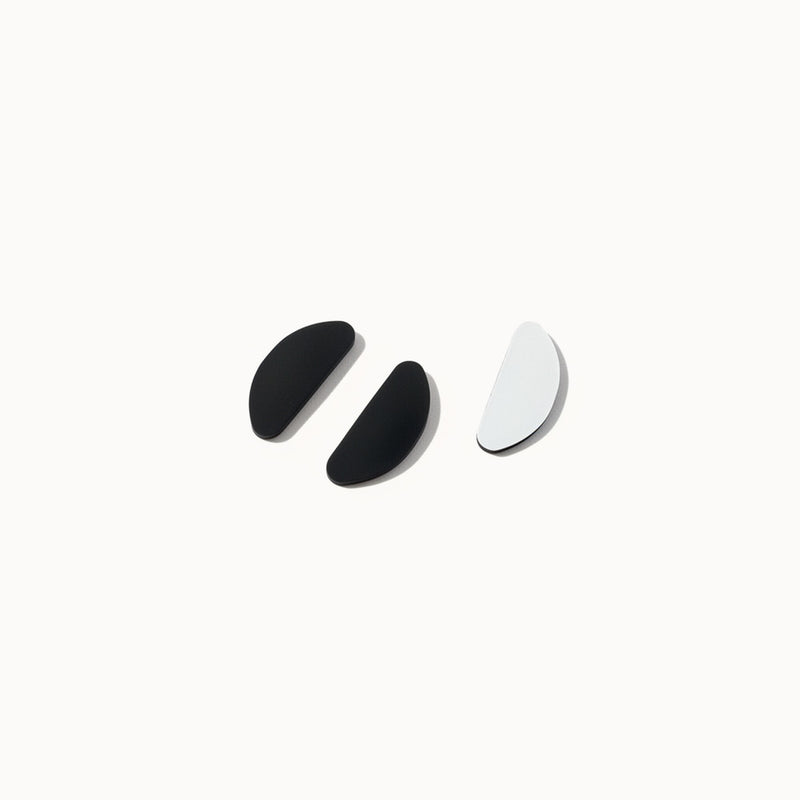 Pair of black adhesive eyeglass nose pads with plain backing sheet