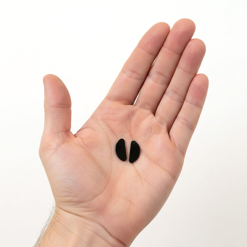 Two black adhesive nose pads held in an open palm to show their small size