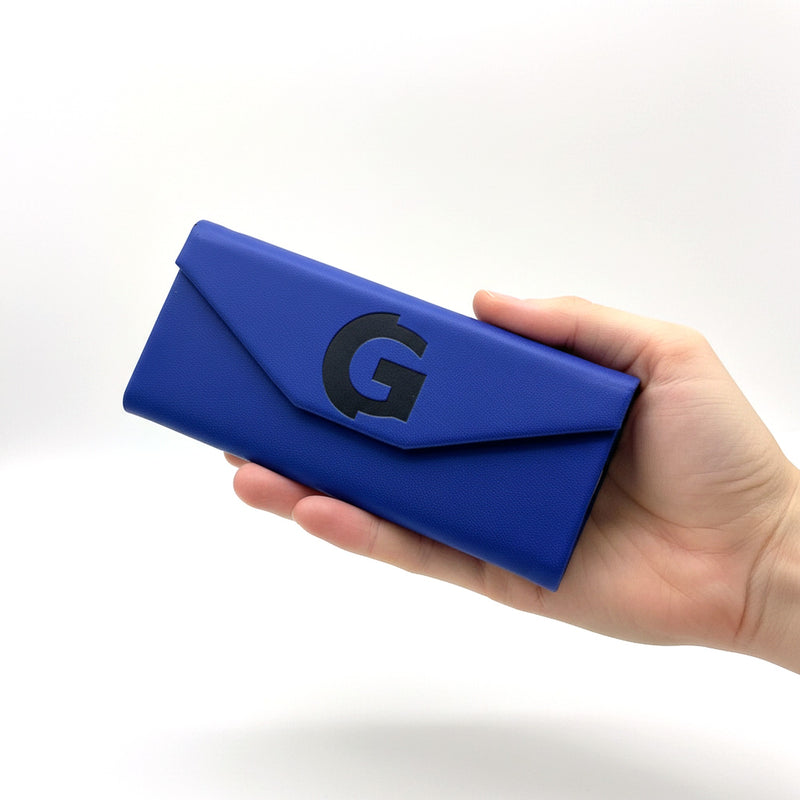 Hand holding the closed cobalt blue GOGHINI fold-up glasses case, G monogram facing forward