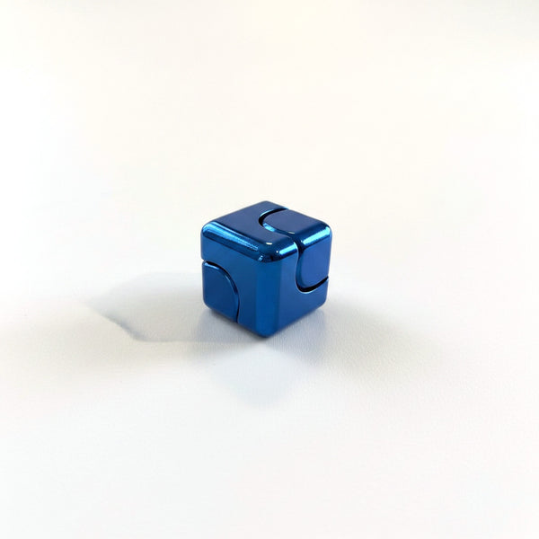Blue anodised metal fidget cube resting on a corner edge, curved seam visible